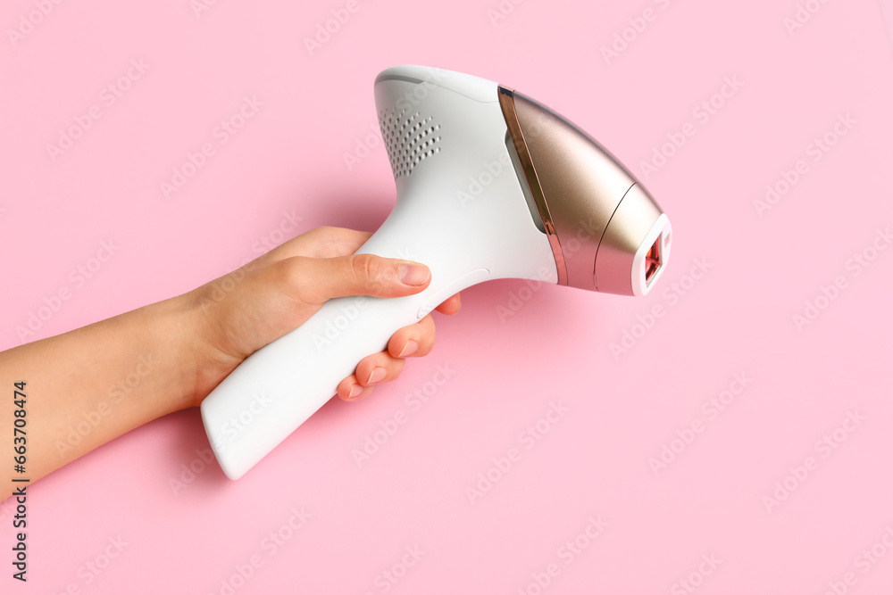 Female hand with modern photoepilator on pink background