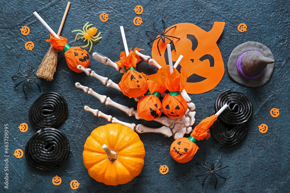 Composition with tasty lollipops, skeleton hand and Halloween decor on dark background