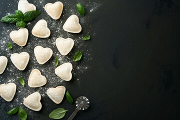 Italian ravioli pasta in heart shape. Tasty raw ravioli with flour and basil on dark background. Food cooking ingredients background. Valentines or Mothers Day lunch ideas. Top view with copy space.