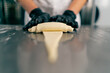 Close-up of the chef's gloved hands shaping and twisting raw dough into shape of croissants for baking