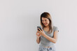 Asian Thai woman wear grey, happy smiling while using and looking at smartphone, texting and chatting with someone, isolated over white background.