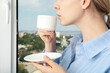 © Atlas - A woman drinks coffee near an open window with a view of the city
