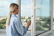 © Atlas - A woman drinks coffee near an open window with a view of the city