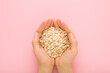 Young adult woman hands holding dry rolled oat on light pink table background. Pastel color. Closeup. Point of view shot. Healthy food. Top down view.