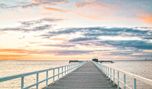 Long Wooden Pier With Iron Fences Near Sea At Sunset