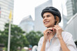 Businesswoman putting cycling helmet prepared go to work at office. Close up female smile and wearing helmet safety ride bicycle on street in city. eco-friendly vehicle, sustainable lifestyle concept