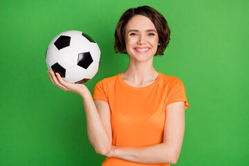 Sticker - Photo of charming lady arm hold football toothy smile look camera isolated on green color background