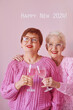 Two mature women in pink sweaters, drinking wine and celebrating 