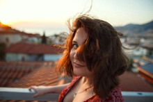 Outdoor Portrait Of Young Pretty Sensual Girl Posing At Roof At Sunset. Fluing Hair On Wind. View On Mediterranian City Buildings And Red Roofs