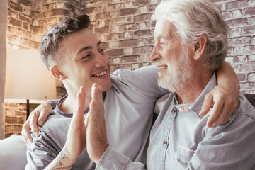 Wall Mural - Young boy and his grandfather smile as they high five each other while sitting on the sofa at home, old and new generation - caring for the people we love