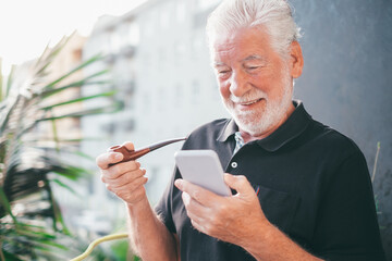 Wall Mural - Portrait of Smiling Handsome Senior Bearded Man Smoking Pipe Outdoor On the Home Balcony Using Mobile Phone for Tech and Social