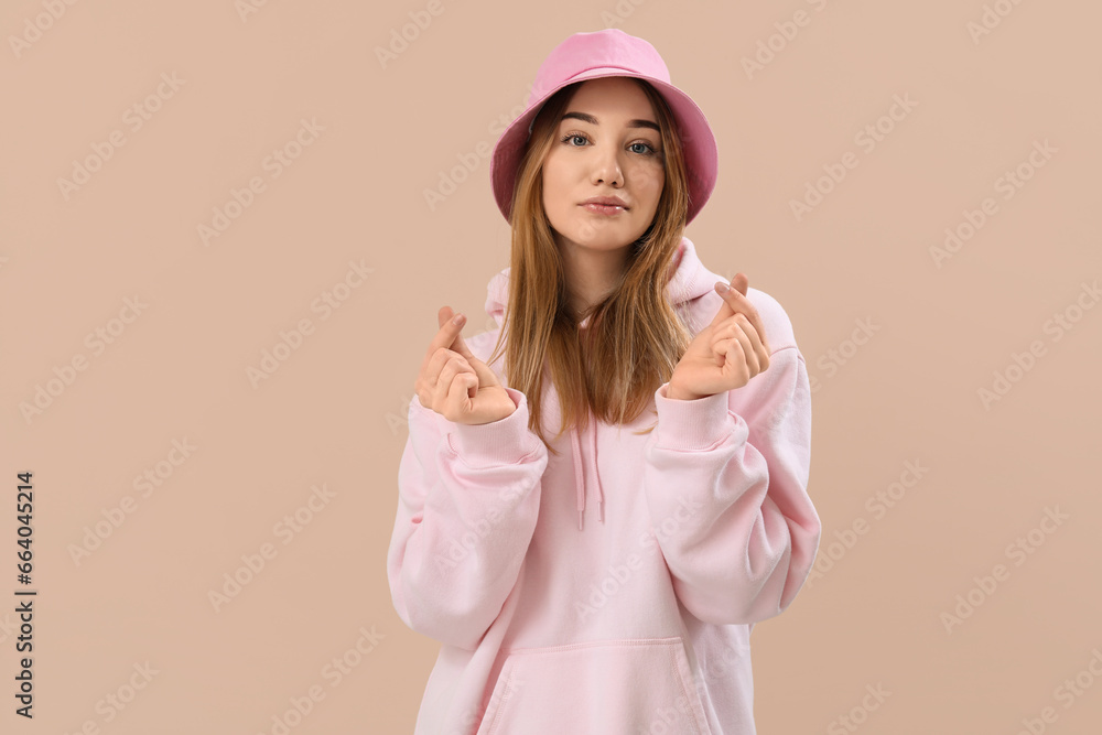 Young woman making heart with her fingers on beige background