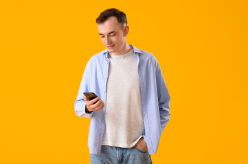 Young man with mobile phone messaging on yellow background