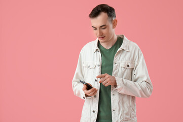 Young man with mobile phone messaging on pink background