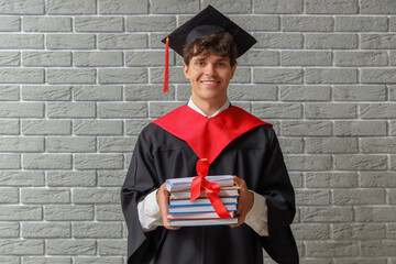 Poster - Male graduate student with diploma and books on grey brick background