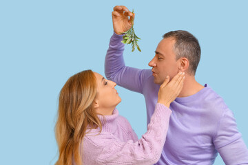 Wall Mural - Mature couple kissing under mistletoe branch on blue background