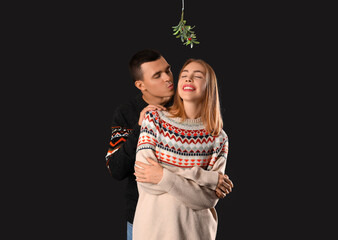 Canvas Print - Young couple kissing under mistletoe branch on dark background