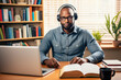 An African American man wearing headphones sits in front of a monitor and books. Remote learning, work