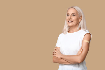 Mature woman with medical patch on arm against beige background. Vaccination concept