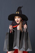 Surprised young woman in witch hat with black shopping bags. Seasonal discounts. Halloween sale. Dark background. Black friday
