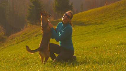 Wall Mural - CLOSE UP: Smiling young woman hugs her adorable brown dog with a wagging tail