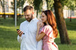 © CinemaF - Concept of happy family at the park. Young man using smartphone while his girlfriend hugs him. Husband browsing social medias with wife when they resting on picnic. Happy couple watching their photos