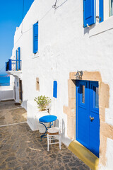 Wall Mural - Typical white Greek house with blue door and small table with chair on narrow street in Plaka village, Milos island, Cyclades, Greece