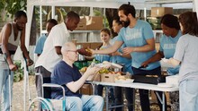 Charity Organization Shows Devotion To Fighting Hunger And Poverty By Giving Away Free Meals To Homeless People. Warm Food Is Provided By Volunteers To Caucasian Wheelchair User And Less Privileged.