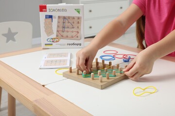 Wall Mural - Motor skills development. Girl playing with geoboard and rubber bands at white table indoors, closeup