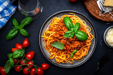 Wall Mural - Spaghetti bolognese or pasta with minced meat and tomato sauce with green basil leaves on black table background, top view