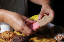 Woman's Hand Taking A Piece Of Mexican Sweet Bread From A White Plate On A Wooden Table. Concept Of Hands Handling Food. Cutting A Three Colors Cookie With Two Hands Horizontal.