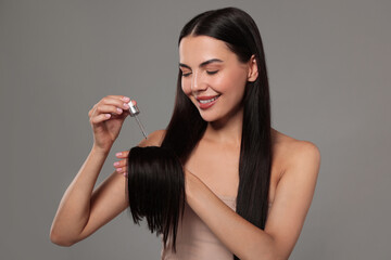 Sticker - Beautiful woman applying hair serum on grey background. Cosmetic product