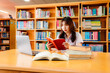 © atsarapong - Asian female university student sitting at table with books and laptop in library