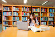 © atsarapong - Asian female university student sitting at table with books and laptop in library