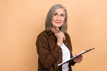 Poster - Portrait of creative minded lady hold clipboard pen touch chin look empty space isolated on beige color background