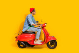 Full body photo of attractive young man driving ride retro red moped dressed stylish jeans clothes isolated on yellow color background