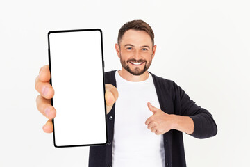 Wall Mural - Handsome young man holding a smartphone mockup with a blank screen and smiling on an orange background.