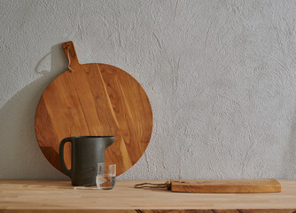 Wooden cutting board on the table, kitchenware, vase of plant grey decorative wall background.