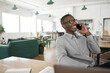 © mavoimages - Smiling young African businessman talking on his phone at work