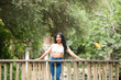 © @skuder_photographer - Young and beautiful brunette woman and latin, leaning on the railing of the wooden bridge over the duck and fish pond in the park. The woman is smiling and happy and enjoying the day.