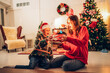 © kelvn - Family is celebrating at home before Christmas. Happy boy and girl are giving themselves Christmas gifts sitting on floor next to Xmas tree.
