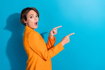 Side photo of young surprised crazy business lady wearing orange jacket point fingers mockup promo sale isolated on blue color background