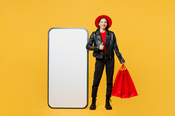 Wall Mural - Full body young woman in casual clothes red hat hold shopping package bags big huge blank screen mobile cell phone show thumb up isolated on plain yellow background Black Friday sale buy day concept