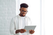 © VisualProduction - African american man using a mobile tablet with smart home. A handsome young man standing in the kitchen, using a mobile tablet.