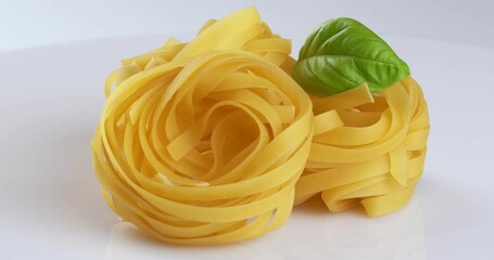 Canvas Print - Close-up footage of a raw tagliatelle pasta with basil on the rotating table on the white background.