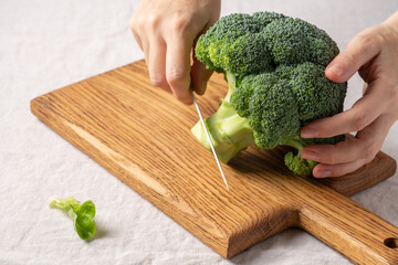 Wall Mural - Female hands cutting head of broccoli with knife on cutting board. Cooking food close up view