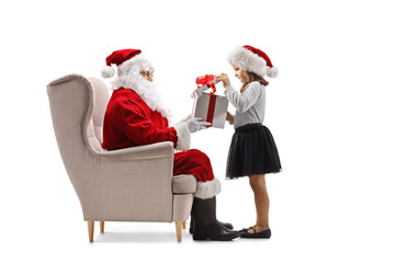 Wall Mural - Santa claus sitting in an armchair and girl opening a present box