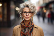 Stylish smiling middle-aged woman on a city street. Portrait of a lady with a gray hairstyle, wearing glasses and outerwear outdoors, looking at camera
