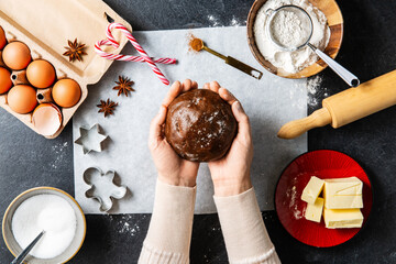 Wall Mural - baking, cooking and christmas concept - close up of hands holding gingerbread dough and ingredients on black kitchen table top