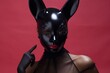 Young woman in black tulle costume with red lips and black latex bunny mask against a red wall